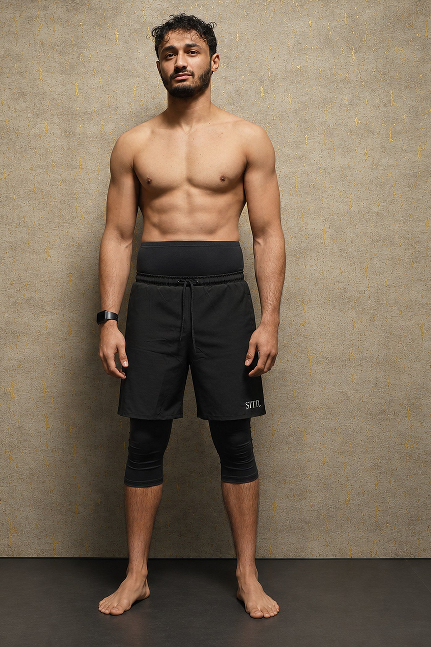 Model draagt de zwarte SITR. 2-in-1 Short, met een losvallende buitenbroek en een aangenaaide compressielegging die doorloopt tot onder de knie