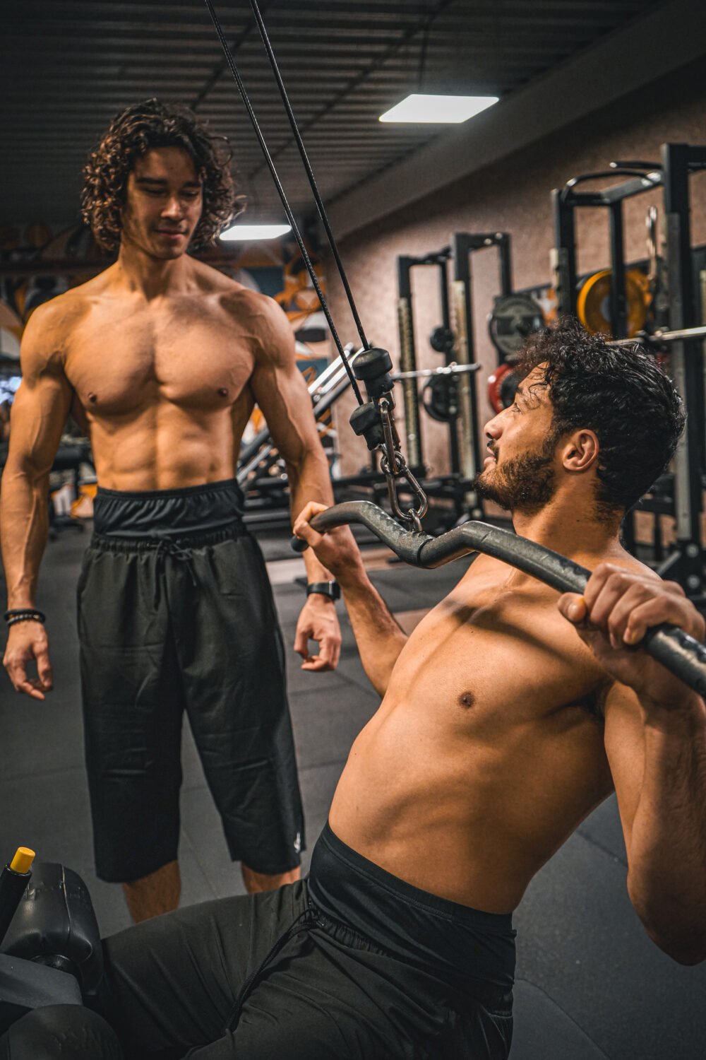 Twee broeders trainen samen aan de kabelmachine, allebei in een zwarte SITR. sportbroek